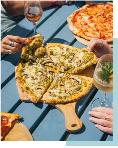 People sharing pizza from a wooden serving board, with glasses of wine on the table.